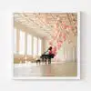 A framed picture captures the Balloon Concerto Piano in a spacious, elegant room with tall windows and a coffered ceiling. Pink balloons float and cluster around the piano and ceiling, creating a whimsical atmosphere reminiscent of its namesake. The room features light-toned walls and wooden flooring.