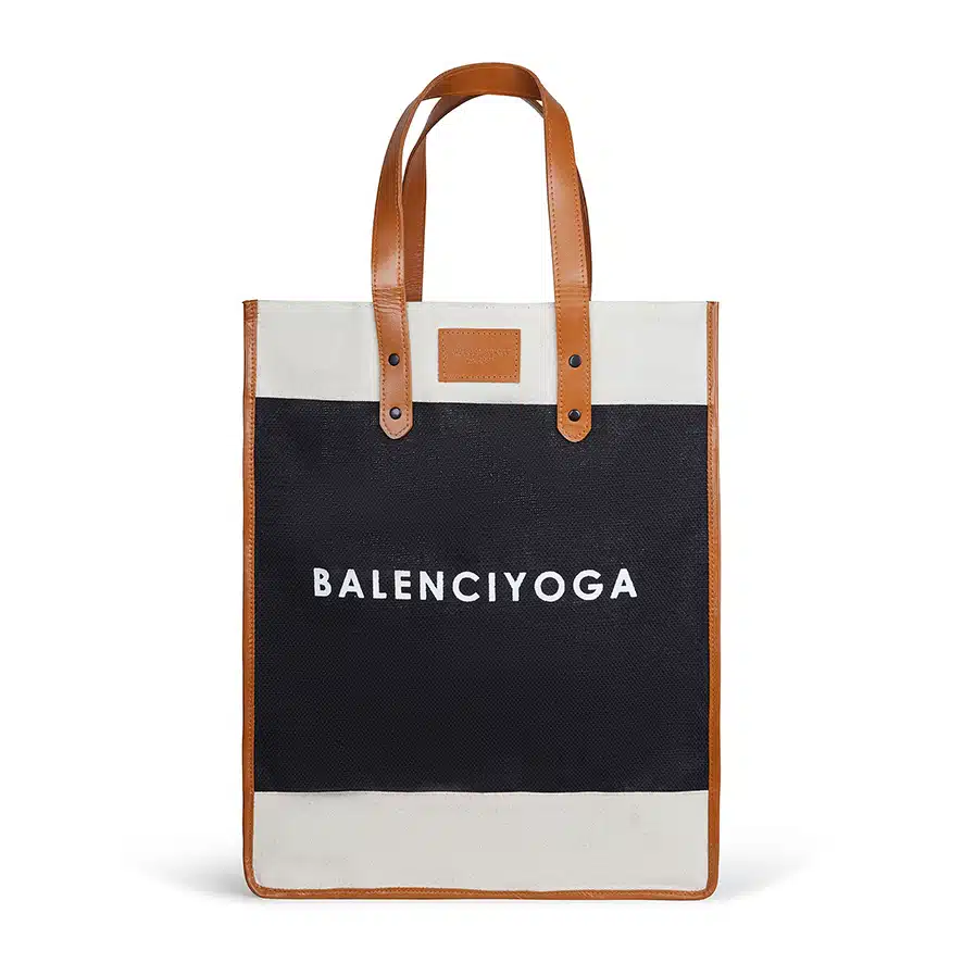 A stylish tote bag with leather handles and trim, featuring a black and white color scheme. The bag proudly displays the bold text "Balenciyoga" on the front.