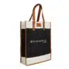 A tall rectangular Bvlgarlic tote bag with brown leather handles and trim. The body of the bag is black and white with the text 