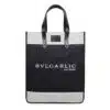 A black and white tote bag with black leather handles. The bag showcases the text 