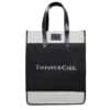 A stylish tote bag featuring black and white color scheme with black leather handles and a rectangular black leather patch near the top. The text 