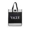 A black and white tote bag with leather handles. The Vague has a rectangular shape and features the word 