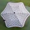 A top view of a large, open Karen Walker Umbrella with an octagonal shape and a white, web-like design on a red background, resting on green grass.